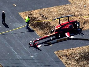 In this image taken from video, authorities look over a helicopter that crash at Taunton Municipal Airport, Tuesday, April 2 2019, in Taunton, Mass. The FAA says the preliminary investigation indicates the helicopter with an instructor and student on board was hovering just above the ground when a gust of wind blew it onto its side. The instructor was piloting it at the time. Both men got out on their own. No names were released. (CBSBoston.com via AP)