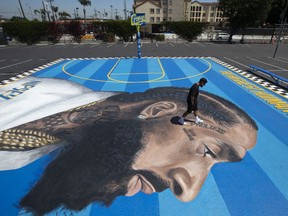 In this April 17, 2019 photo, mural artist Gustavo Zermeno Jr. walks on a basketball court mural he dedicated to slain rapper Nipsey Hussle in Los Angeles. More than 50 colorful murals of Hussle have popped up in Los Angeles since the beloved rapper and community activist was gunned down outside his clothing store.
