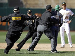 Second base umpire Jeff Nelson (45) grabs a fan that ran onto the field as security guards assist and Oakland Athletics' Stephen Piscotty, right, watches in the ninth inning of a baseball game against the Toronto Blue Jays, Saturday, April 20, 2019, in Oakland, Calif.