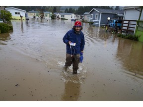 Jett Archuleta wades through a flooded street in the Riverstone Mobile Home Park in Cottage Grove to retrieve medications for his Grandfather Merle Wright and dog treats for Wright's dog Betty Monday, April, 8, 2019 after flood waters rose overnight.