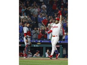 Philadelphia Phillies' Bryce Harper, right, gestures as he scores on his three-run home run, next to Washington Nationals catcher Yan Gomes during the third inning of a baseball game Tuesday, April 9, 2019, in Philadelphia.