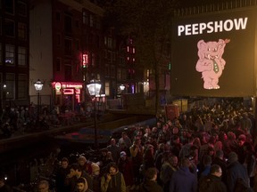 Tourists are bathed in a red glow emanating from the windows and peep shows' neon lights are packed shoulder to shoulder as they shuffled through the alleys in Amsterdam's red light district, Netherlands, Friday evening, March 29, 2019.  The Dutch capital plans to ban guided tours of the red light district, saying they are disrespectful and contribute to congestion in the narrow, canal-side streets where scantily-clad sex workers sit behind windows to attract customers.