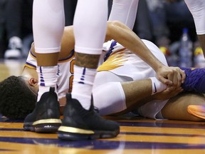 An injured Phoenix Suns guard Devin Booker holds his ankle after turning it during the first half of the team's NBA basketball against the Utah Jazz on Wednesday, April 3, 2019, in Phoenix.