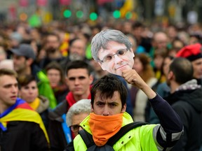 A protester holds aloft a mask of Catalonia's former president Carles Puigdemont during a demonstration in Barcelona on March 25, 2018.