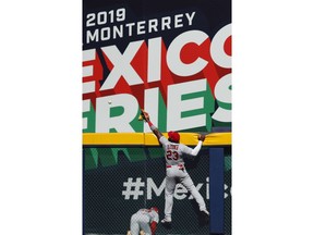 St. Louis Cardinals' Marcell Ozuna leaps but can't stop a 3-run home run by Cincinnati Reds' Jesse Winker during the fifth inning of a baseball game in Monterrey, Mexico, Sunday, April 14, 2019.