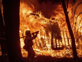 FILE - In this Nov. 9, 2018 file photo, firefighter Jose Corona sprays water as flames from the Camp Fire consume a home in Magalia, Calif. The massively expensive wildfires in 2017-2018 have prompted the creation of a five-member board, that met Wednesday April 3, 2019, to continue to consider who should pay for the increasingly destructive and costly wildfires.