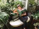 A woman reads amongst plants. 