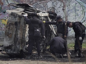 Police review the charred remains of a car that exploded as authorities were responding to a report of a vehicle with a corpse inside, in the San Bartolo neighborhood of Soyapango, El Salvador, Monday, April 29, 2019. Two police officers were injured in the explosion.