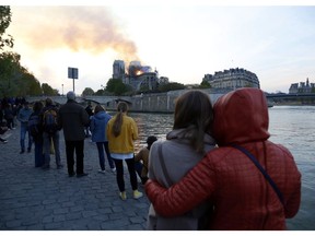 People watch as flames and smoke rise from Notre Dame cathedral as it burns in Paris, Monday, April 15, 2019. Massive plumes of yellow brown smoke is filling the air above Notre Dame Cathedral and ash is falling on tourists and others around the island that marks the center of Paris.