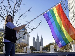 FILE - In this Nov. 14, 2015 file photo, Sandy Newcomb poses for a photograph with a rainbow flag as people gather for a mass resignation from The Church of Jesus Christ of Latter-day Saints in Salt Lake City. The Church of Jesus Christ of Latter-day Saints is repealing rules unveiled in 2015 that banned baptisms for children of gay parents and made gay marriage a sin worthy of expulsion. The surprise announcement Thursday, April 4, 2019, by the faith widely known as the Mormon church reverses rules that triggered widespread condemations from LGBTQ members and their allies.