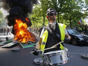 A man bangs a drum in front of a fire on the street during a yellow vest demonstration in Paris, Saturday, April 20, 2019. French yellow vest protesters are marching anew to remind the government that rebuilding the fire-ravaged Notre Dame Cathedral isn't the only problem the nation needs to solve.