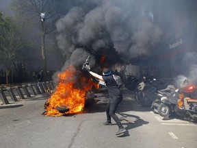 A protestor throws a scooter onto a pile of burning motorbikes during a yellow vest demonstration in Paris, Saturday, April 20, 2019. French yellow vest protesters are marching anew to remind the government that rebuilding the fire-ravaged Notre Dame Cathedral isn't the only problem the nation needs to solve.