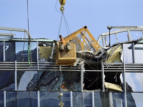 With a portion of the broken crane on the roof behind, a worker suspended in a basket clears debris from a building damaged when the crane atop it collapsed a day earlier, Sunday, April 28, 2019, in Seattle. The construction crane fell from a building on Google's new campus during a storm that brought wind gusts, crashing down onto one of the city's busiest streets and killing multiple people.