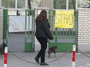 A woman walks by a school where teachers are taking part in nationwide pay strike, with banners declaring the participation in the strike and also parent's support for it, in Warsaw, Poland, Monday, April 15, 2019. The right-wing government says it has money only to grant half of the teachers' demands in a sign that its policy of pre-election spending has reached its limit.