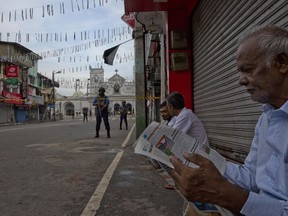 A man reads a newspaper as air force officers stand guard outside St. Anthony's Shrine in Colombo, Sri Lanka, Friday, April 26, 2019.