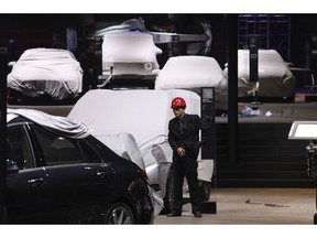 A worker stands near covered vehicles in a hall of the Auto Shanghai 2019 show in Shanghai on Monday, April 15, 2019. This year's Shanghai auto show highlights the global industry's race to make electric cars Chinese drivers want to buy as Beijing winds down subsidies that promoted sales.
