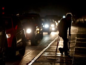 FILE - In this March 29, 2019 file photo, a man on crutches is illuminated by headlights of oncoming traffic, in Caracas, Venezuela. Venezuelans are struggling to understand the Sunday, March 31, 2019 announcement that the nation's electricity is being rationed to combat daily blackouts.