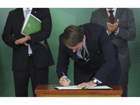 FILE - In this Jan. 15, 2019 file photo, Brazilian President Jair Bolsonaro signs a decree that loosens restrictions on gun ownership, as an anti-crime move, at Planalto presidential palace in Brasilia, Brazil. Before, non-military or police who wanted to own a gun had to justify their interest as part of the process, and now wide categories of people will qualify, like those in rural areas, or urban areas with high levels of homicide, business owners, gun collectors and hunters.