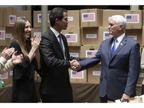 FILE - In this Feb. 25, 2019 file photo, Venezuela's self-proclaimed interim president Juan Guaido, center, accompanied by his wife Fabiana Rosales, shakes hands with Vice President Mike Pence in a room filled with humanitarian aid destined for Venezuela, in Bogota, Colombia. Guaido, whom 50 countries recognize as Venezuela's rightful leader, has tried to control the distribution of U.S-supplied aid in a bid to weaken Nicolas Maduro's grip on power.