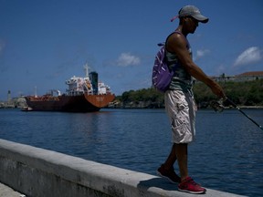 A fisherman walks on the Malecon seawall where an oil tanker can be see in the background in Havana, Cuba, Wednesday, April 17, 2019. Washington has sanctioned Venezuela's oil industry and shipping companies that move Venezuelan oil to Cuba.