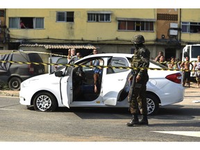 The body of Evaldo dos Santos Rosa sits slumped over inside his car as a soldier stands guard nearby in the Guadalupe neighborhood, Rio de Janeiro, Brazil, Sunday, April 7, 2019. Authorities say soldiers mistook the car driven by Santos Rosa for that of criminals and was hit by 80 shots fired by members of the armed forces. Rosa was killed and his wife's stepfather wounded. Relatives say his wife, 7-year-old son and another woman were unharmed.