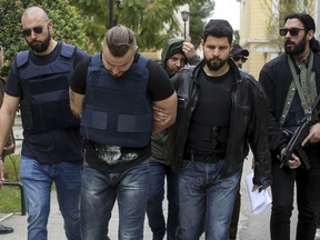 Plain clothed policemen escort a Bulgarian man, center, at a court in Athens, Friday, April 5, 2019. Greek authorities said Friday they have arrested and charged a Bulgarian man over the suspected contract killing of a Greek-Australian who was fatally shot outside his home in an Athens seaside suburb last year.