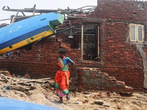 An Indian woman walks next to a damaged building with a fishing boat lodged on its roof along the seafront in Puri in the eastern Indian state of Odisha.