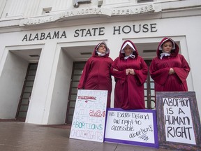 FILE - In this Wednesday April 17, 2019 file photo, Bianca Cameron-Schwiesow, from left, Kari Crowe and Margeaux Hardline, dressed as handmaids, take part in a protest against HB314, the abortion ban bill, at the Alabama State House in Montgomery, Ala. An attempt to outlaw abortion in Alabama is headed to a committee vote in the Alabama Senate. The Senate Judiciary Committee will vote Wednesday morning, May 8, 2019, on the bill following a public hearing.