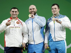 File - In this Monday, Aug. 15, 2016 file photo, Ruslan Nurudinov, of Uzbekistan, center, holds his gold medal as he is joined by silver medalist Simon Martirosyan, of Armenia, left, and bronze medalist Alexandr Zaichikov, of Kazakhstan, right, during the medal ceremony for the men's 105 kg weightlifting event at the 2016 Summer Olympics in Rio de Janeiro, Brazil. Nurudinov has been disqualified from the 2012 London Games for doping with an anabolic steroid. The Court of Arbitration for Sport says its new anti-doping chamber stripped Nurudinov of fourth place in London in the 105-kilogram weight class. The 27-year-old lifter from Uzbekistan now faces a ban from the International Weightlifting Federation.