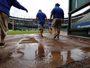 Water lays on the outer track as Texas Rangers grounds crew members head onto the field to remove the tarp after rain showers that delayed the start of a baseball game against the St. Louis Cardinals in Arlington, Texas, Saturday, May 18, 2019.