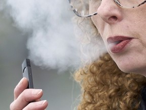 FILE - In this April 16, 2019 file photo, a woman exhales while vaping from a Juul pen e-cigarette in Vancouver, Wash. Schools have been wrestling with how to balance discipline with treatment in their response to the soaring numbers of vaping students. Using e-cigarettes, often called vaping, has now overtaken smoking traditional cigarettes in popularity among students, says the Centers for Disease Control and Prevention. Last year, one in five U.S. high school students reported vaping the previous month, according to a CDC survey.