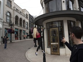 A woman climbs on a street sign to take pictures on Rodeo Drive in Beverly Hills, Calif., on Tuesday, May 7, 2019.