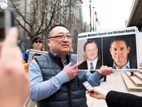 This file picture taken on March 6, 2019 shows Louis Huang of Vancouver Freedom and Democracy for China holding photos of Canadians Michael Spavor and Michael Kovrig, who are being detained by China, outside British Columbia Supreme Court, in Vancouver, as Huawei Chief Financial Officer Meng Wanzhou appears in court.