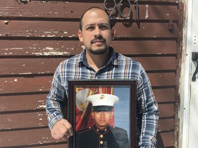 In this April 13, 2019, photo provided by the ACLU of Minnesota, Mark Esqueda poses for a portrait with a photo of him as a U.S.Marine, in Heron Lake, Minn. Esqueda was born in the United States but has been twice denied his request for a passport. He sued the State Department and is asking a federal judge to declare that he is a U.S. citizen.