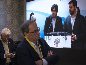 Regional Catalan President Quim Torra, centre, looks at former regional Catalan President Carles Puigdemont appearing on a screen during a video conference from Brussels, at the party headquarters in Barcelona, Catalonia, Spain, Sunday, May 26, 2019. Former Catalan regional president Carles Puigdemont, his ex-No. 2 Oriol Junqueras and former Catalan Cabinet member Toni Comín all won seats for separatist parties in Sunday's EU vote. That's according to provisional results released by Spain's Interior Ministry with 85% of the votes counted.