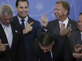 Lawmakers make finger-gun hand gestures as Brazil's President Jair Bolsonaro signs a second decree that eases gun restrictions, at Planalto presidential palace in Brasilia, Brazil, Tuesday, May 7, 2019. The decree opens Brazil's market to guns and ammunition made outside of Brazil according to a summary of the decree. Gun owners can now buy between 1,000 -5,000 rounds of ammunition per year depending on their license, up from 50 rounds. Lower-ranking military members can now carry guns after 10 years of service.