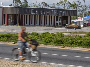 In this May 3, 2019 photo, a cyclist rides by a building damaged by Hurricane Michael in Parker, Fla. Residents in these parts of the Florida Panhandle that were devastated by Hurricane Michael six months ago hope President Donald Trump gets a glimpse of the continuing suffering in the region when he arrives for a campaign rally this week.