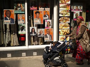 A woman walks past political campaign posters placed on a restaurant window at the African Matonge quarter in Brussels, Wednesday, May 22, 2019. Belgium, which has one of the oldest compulsory voting systems, will go to the polls for regional, federal and European elections on May 26, 2019.