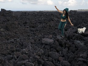 In this Monday, April 22, 2019 photo, Tisha Montoya and her dog Bebe cut through the lava field that covered much of her property and destroyed her home near Pahoa, Hawaii. Tisha and her father Edwin Montoya lived on the secluded property for many years until they had to evacuate due to the 2018 Kilauea lava eruption where the molten rock eventually took nearly all the structures, including the home and all but one small chicken coop that Edwin built.