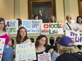 FILE - In this Friday, March 22, 2019, file photo, pro-abortion rights and anti-abortion demonstrators display their signs in the lobby of the Georgia State Capitol building during the 35th legislative day at the Georgia State Capitol building in downtown Atlanta. Georgia Gov. Brian Kemp is set to sign legislation on Tuesday, May 7, 2019, banning abortions at around six weeks of pregnancy, before many women know they're pregnant.