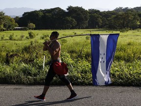 FILE - In this Oct. 25, 2018 file photo, a Honduran migrant carries his national flag as he walks north as part of a thousands strong caravan trying to reach the U.S., still over 1000 miles away, near Mapastepec, Mexico. Fleeing violence, poverty, corruption and chaos, thousands of Hondurans continue to flee despite the dangers and uncertain prospects even if they make it to the U.S.