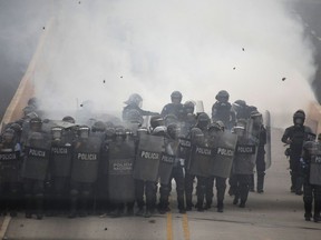 Police stand behind their shield as demonstrators throw rocks at them during a protest against the government of President Juan Orlando Hernandez, in Tegucigalpa, Honduras, Friday, May 31, 2019. Protesters are demanding the government revoke decrees that they say would lead to massive, uncompensated layoffs of public employees and the privatization of state hospitals.