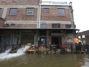 Workers stand near the back entrance of the 1/2 Nelson restaurant as pumps continue pumping flood water from the basement of the new Davenport business Thursday, May 2, 2019. The Mississippi River is expected to reach a record level of 22.7 feet Thursday night.