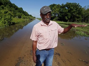 In this Thursday, May 23, 2019 photo, Larry Walls, a farmer and businessman stands at the edge of a backwater flooded road leading to his 560 acres of rented farm land near Louise, Miss. Walls can no longer drive to the property without the possibility of getting flooded or stuck. Four months into what seems like a never-ending flood, he's been trying to stay busy. He pressure-washed his church, and he's been shooting the snakes that slither out of a swollen creek submerging his backyard.