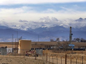FILE - In this Feb. 13, 2017 file photo, a petroleum industry storage tank borders a ranch, left, near a drilling rig, right, with the Front range of the Rocky Mountains rising up in the background, near Mead, Colo. A federal judge said Wednesday, May 29, 2019, U.S. officials must consider the climate change effects from leasing about 250 square miles of public lands in Colorado and Utah for oil and gas exploration.