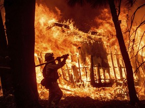 FILE - In this Nov. 9, 2018 file photo, firefighter Jose Corona sprays water as flames from the Camp Fire consume a home in Magalia, Calif. Federal officials say an effort to develop a better fire shelter following the deaths of 19 wildland firefighters in Arizona six years ago has failed. Officials at the National Interagency Fire Center in Boise in a decision on Wednesday, May 15, 2019 say the current fire shelter developed in 2002 will remain in use, saying the current shelter combines the most practical level of protection balanced against weight, bulk and durability.