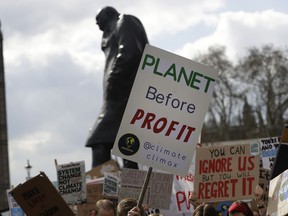 FILE - In this Friday, April 12, 2019 file photo, climate change demonstrators hold banners in front of the Winston Churchill Statue during a protest near Parliament in London. An independent committee that advises the British government on climate change says the UK should target net-zero emissions of greenhouse gases by 2050, recommending the rapid adoption of policies to change everything from how people heat their homes to what they eat. The report released Thursday, May 2 by the Committee on Climate Change stresses that it is time for ambitious goals to curb the emissions that cause climate change.