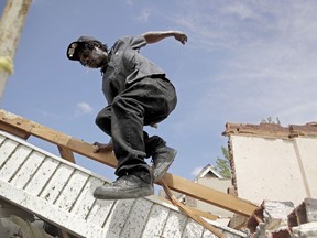 Tavaris McClain, left, jumps off a pile of debris as he cleans up outside his mother's destroyed home Thursday, May 23, 2019 after a tornado tore though Jefferson City, Mo. late Wednesday.