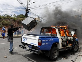 A man throws a bin at a torched police vehicle during a protest against the government of Honduras' President Juan Orlando Hernandez, in Tegucigalpa, Honduras, Thursday, May 30, 2019. Thousands of doctors and teachers have been marching through the streets of Honduras' capital for the last three weeks against presidential decrees they say would lead to massive public sector layoffs.