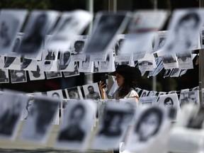 Framed by images of people who have been disappeared, a woman takes photos during a Mother's Day march in Mexico City, Friday, May 10, 2019. Mothers and other relatives of persons gone missing in the fight against drug cartels and organized crime are demanding that authorities locate their loved ones.